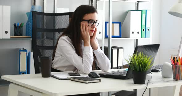 Woman Propping Head in Hand and Using Laptop in Modern Office