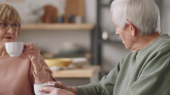 Senior Woman Reading News Online and Talking with Husband over Tea alt