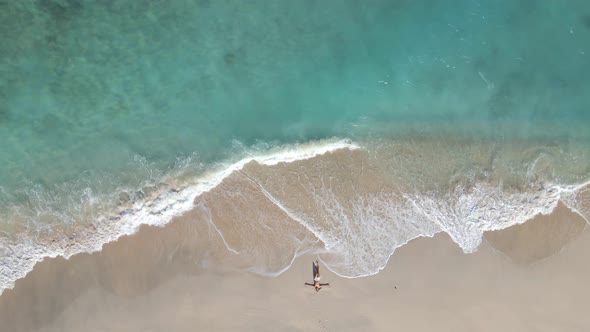 Aerial top down of relaxing woman at seashore and crystal clear water of Gili meno Island during sun alt