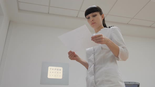 The ophthalmologist looks at the table on the wall alt