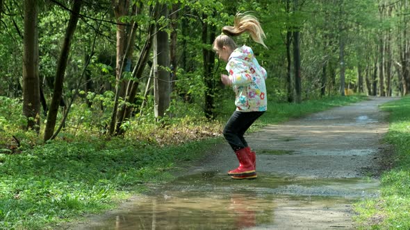 Happy cute little girl jumping in puddle after rain in spring