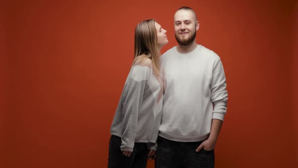 Couple in Love Man and Woman Kissing Each Other in Cheeks on Red Background alt