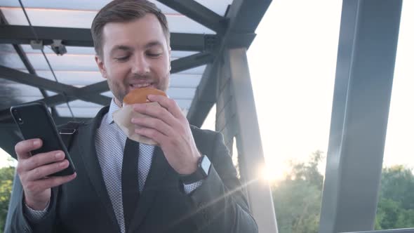 Young Manager Eating Fast Food During Lunch Break Outdoors on the Way to Work alt