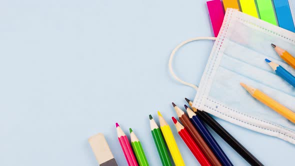 School Supplies with a Notepad Lie on a Pastel Blue Background with a Medical Mask alt