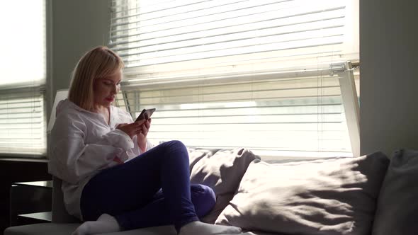 Woman Is Relaxing in Her Home in Weekend Time, Sitting on Couch and Using Smartphone with Wifi alt
