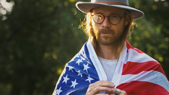 Young Guy in Glasses and Hat is Putting on Flag of USA on His Shoulders