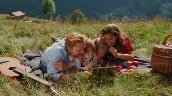 Family Holding Tablet Picnic Lying Grass Mountain Hill alt