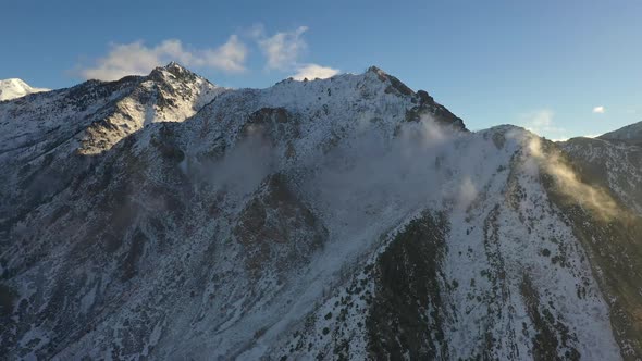 Mountain tops covered in snow with thin clouds rolling off alt