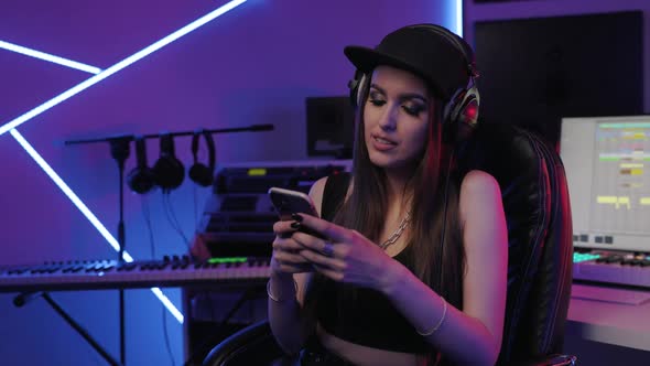Woman in Recording Studio Sits on a Chair with Smarphone in Hands alt