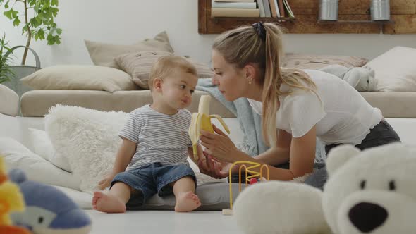 Happy and smiling mom makes your beautiful child baby eat banana
