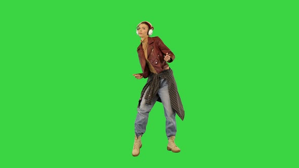 Young Girl in Stylish Clothes Starts to Dance While Listening to Music with Headphones on a Green alt