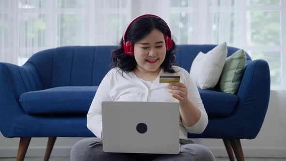 plus-size woman is happily using her online shopping credit card in her room.