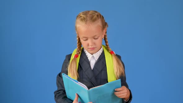 Happy teenager schoolgirl in a school uniform with a backpack reads a book
