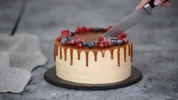 Female Hands Cutting Delicious Caramel Cake with Frozen Summer Berries