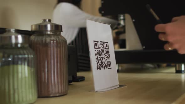Close up of female hand holding smartphone, scanning qr code at countertop alt