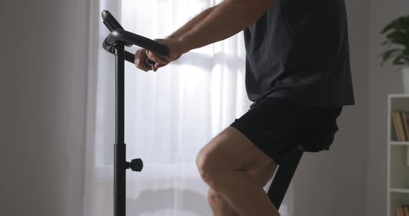 Adult Sportsman Is Training on Stationary Bike at Home Closeup of Body Caring About Health Keeping alt
