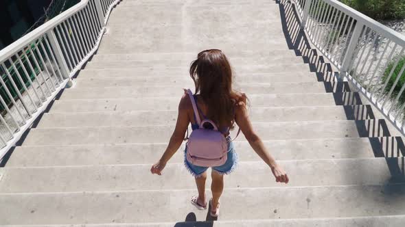 Happy Playful Woman Coming down the stairs with a backpack. Slow motion alt