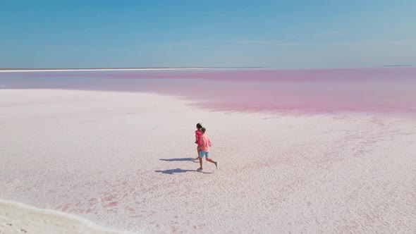 Aerial Drone Footage of Happy Young Couple in Pink Wear Having Fun and Joyfully Running on White alt