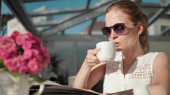 Young Woman with Ponytail and Sunglasses Is Drinking Coffee in the Restaurant