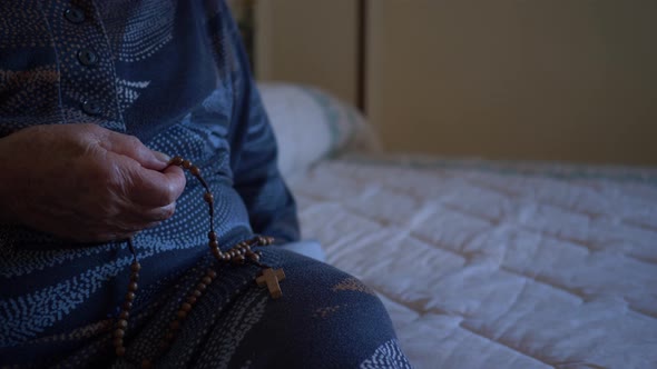 Elderly woman 70-80 years old prays with the rosary at home.