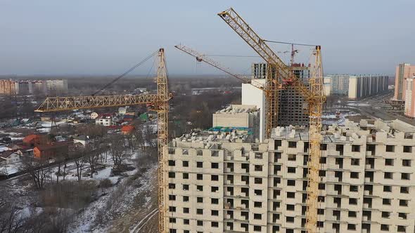 Three Cranes Work on the Construction Site of a Brick High-rise. Aerial View of the Construction of