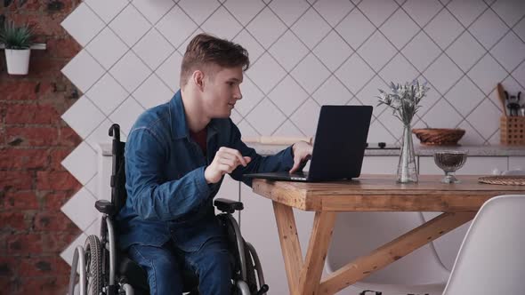 Man in Wheelchair Working with Laptop at Home. Adult Disabled Male Working Studying on Laptop