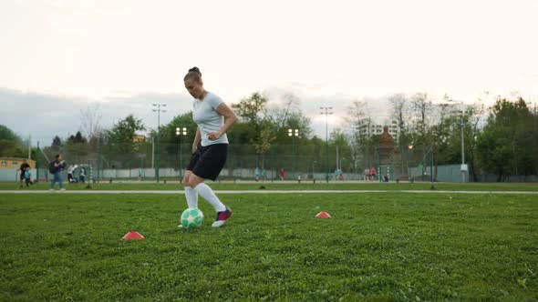 Woman Football Player Practicing on the Grass Field in the the Evening a Freestyler Leads the Ball