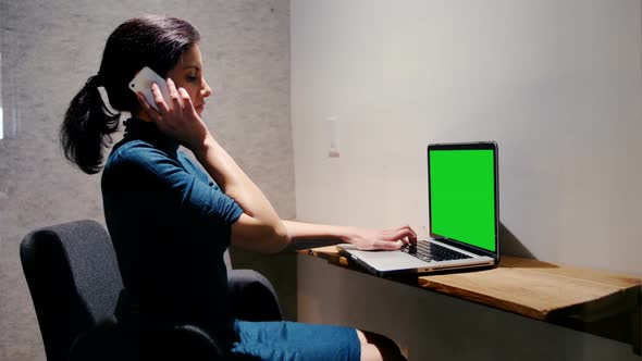 Businesswoman talking on mobile phone while using laptop in a modern office 4 4k alt