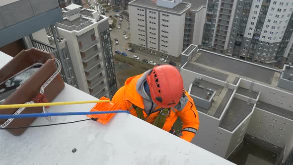 Industrial Climber in Orange Suit and Helmet Prepares To Descend From Roof of Multi-storey Building alt
