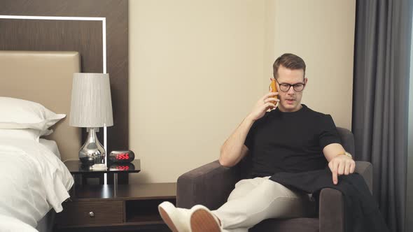Young Businessman Talking on Smartphone with Someone While Sitting in Hotel Room