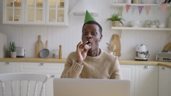 Cheerful Man with Birthday Cap Talks Via Videocall on Laptop alt