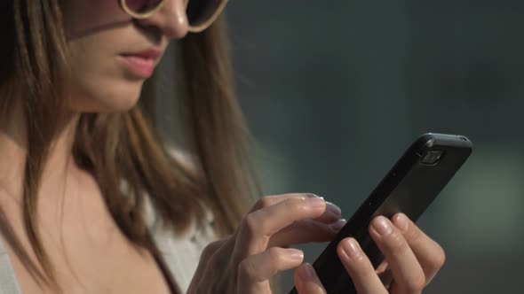 Young Woman in Sunglasses is Typing on a Smartphone Screen