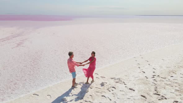 Aerial Epic Drone Image of Lovely Romantic Couple Walking Along Bright Colorful Pink Water of alt