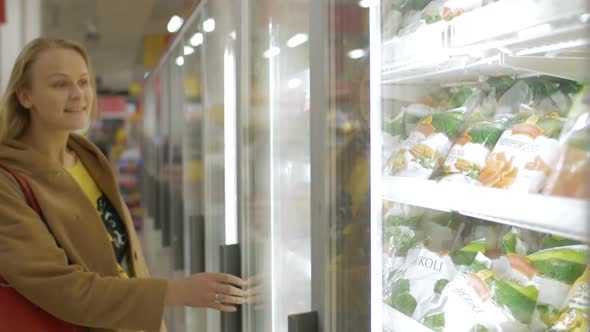 Woman taking frozen product in the shop fridge alt