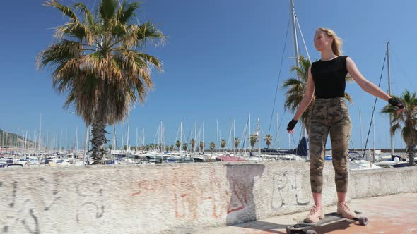 A Beautiful Blonde Girl on Skateboard in Summer Hot Day on Seafront alt
