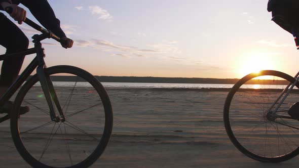 Two Young Men Riding Bicycles on the Beach on the Background of an Orange Sunsetting Sky Slow Motion alt
