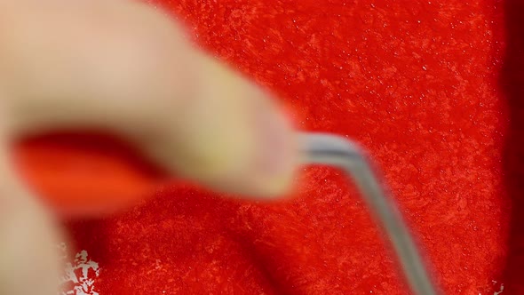 a Hand with a Paint Roller Paints a White Background with Red Paint