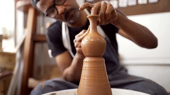 Hands of man at pottery wheel forming clay