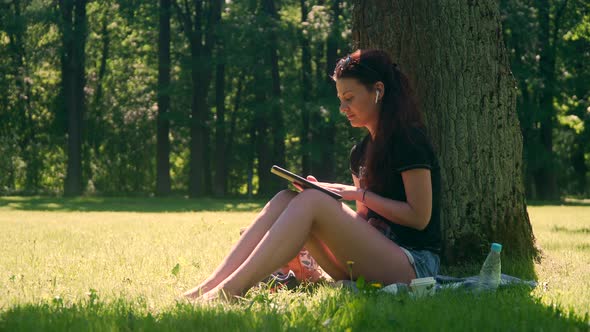 Young Woman In Park Uses Tablet alt