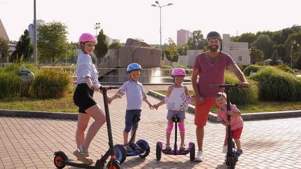 Portrait of Family with Kids on Electric Scooters and Gyro Scooter in the Park alt