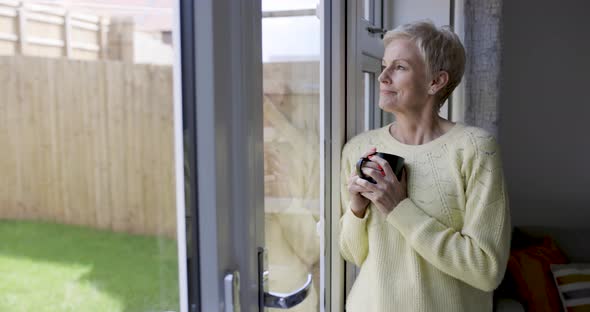 Mature woman holding coffee cup leaning on window