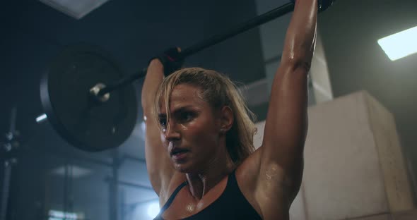 a Female Weightlifter Performs a Barbell Lift in a Dark Gym. a Woman Lifting a Heavy Bar Over Her alt