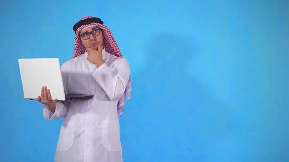 Pensive Arab Man with Laptop on Blue Background alt