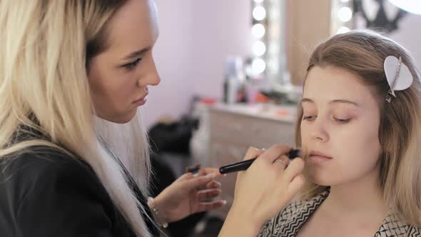 Makeup Artist Is Covering Young Woman's Face with Foundation Cream Using Brush