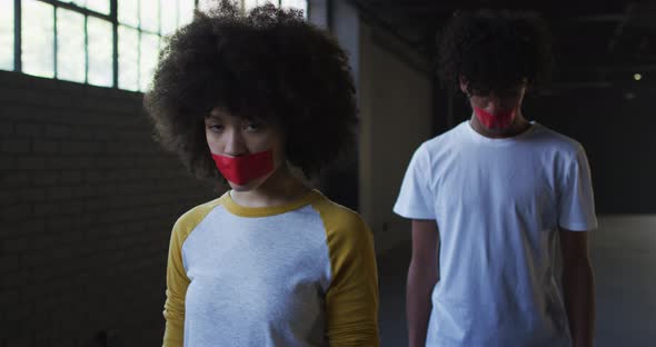 Portrait of african american man and woman with red tape on their mouth in empty parking garage alt
