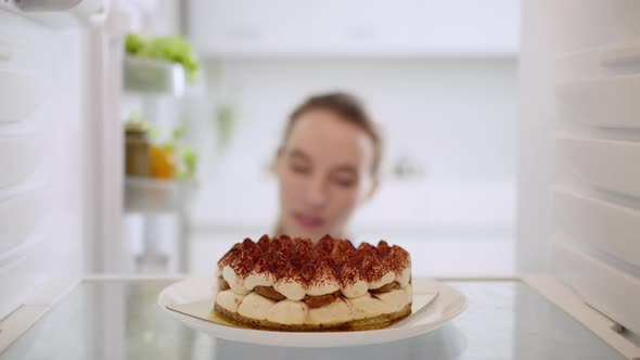 Beautiful woman taking cake from refrigerator. View from inside the working fridge.