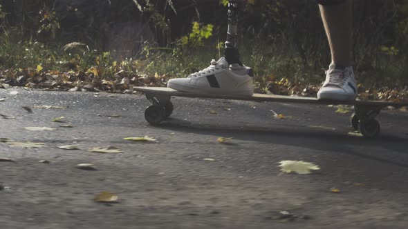 A Young Man with a Metal Prosthetic Leg Rides a Skateboard in an Autumn Park alt