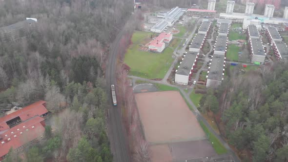 Single Tram Running Through the Suburb Area With Apartments and Forest Aerial alt