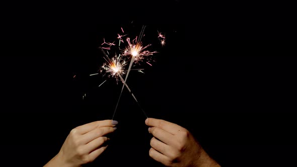 Hands Holding and Waving Bengal Fires. New Year Sparkler Candle Burning on a Black Background alt