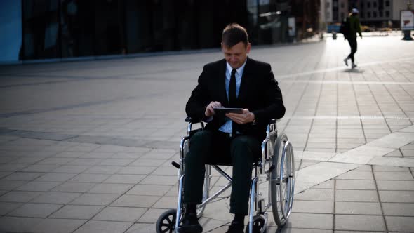 Disabled Businessman Sitting in Wheelchair Outdoor and Work with Tablet PC alt
